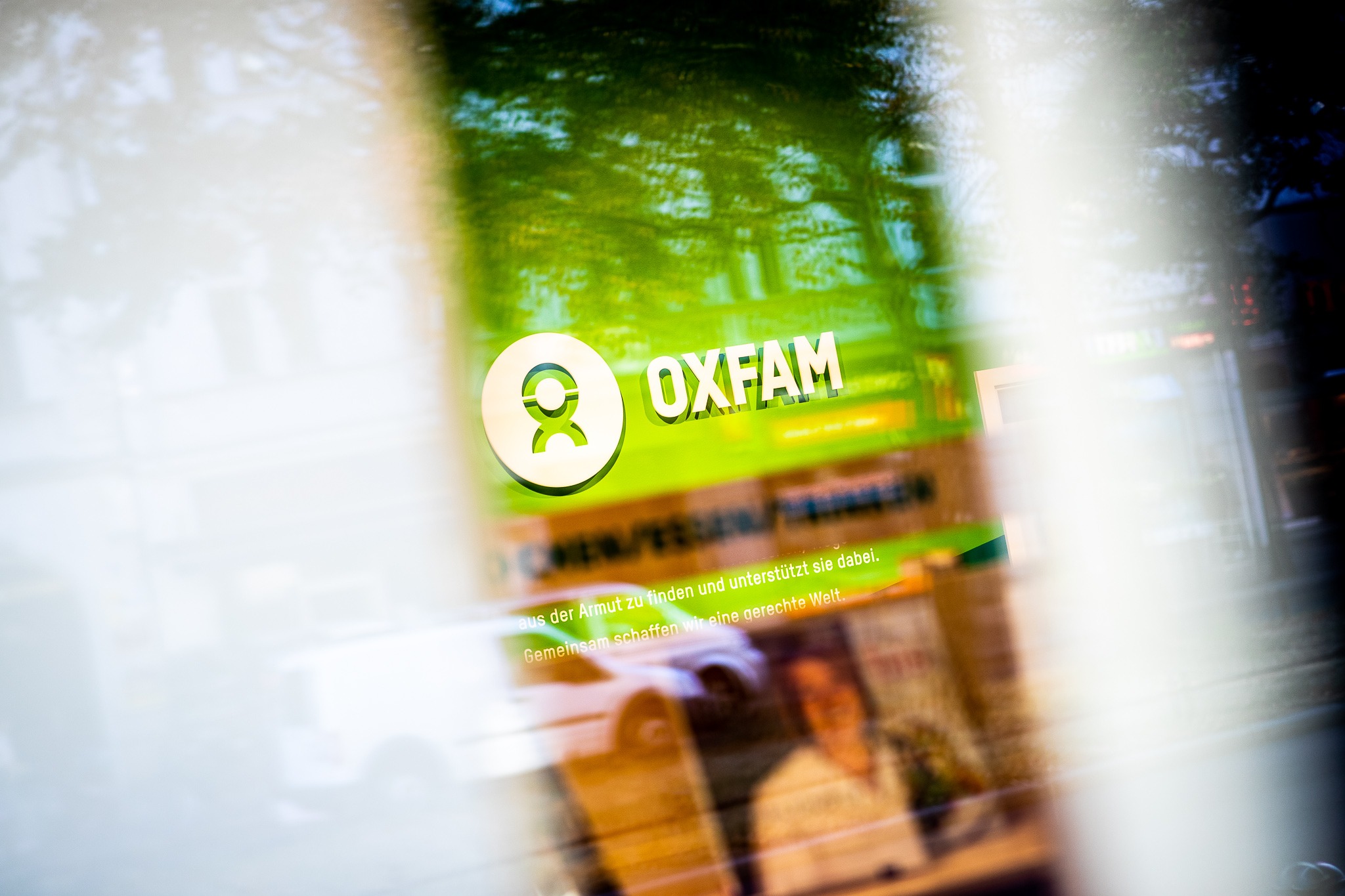 Das Foto zeigt das Logo des Oxfam Deutschland e. V. durch das Schaufenster eines der Ladengeschäfte. Das Foto habe ich im Rahmen der Eröffnung des Geschäfts in Berlin Weissensee für Oxfam fotografiert.