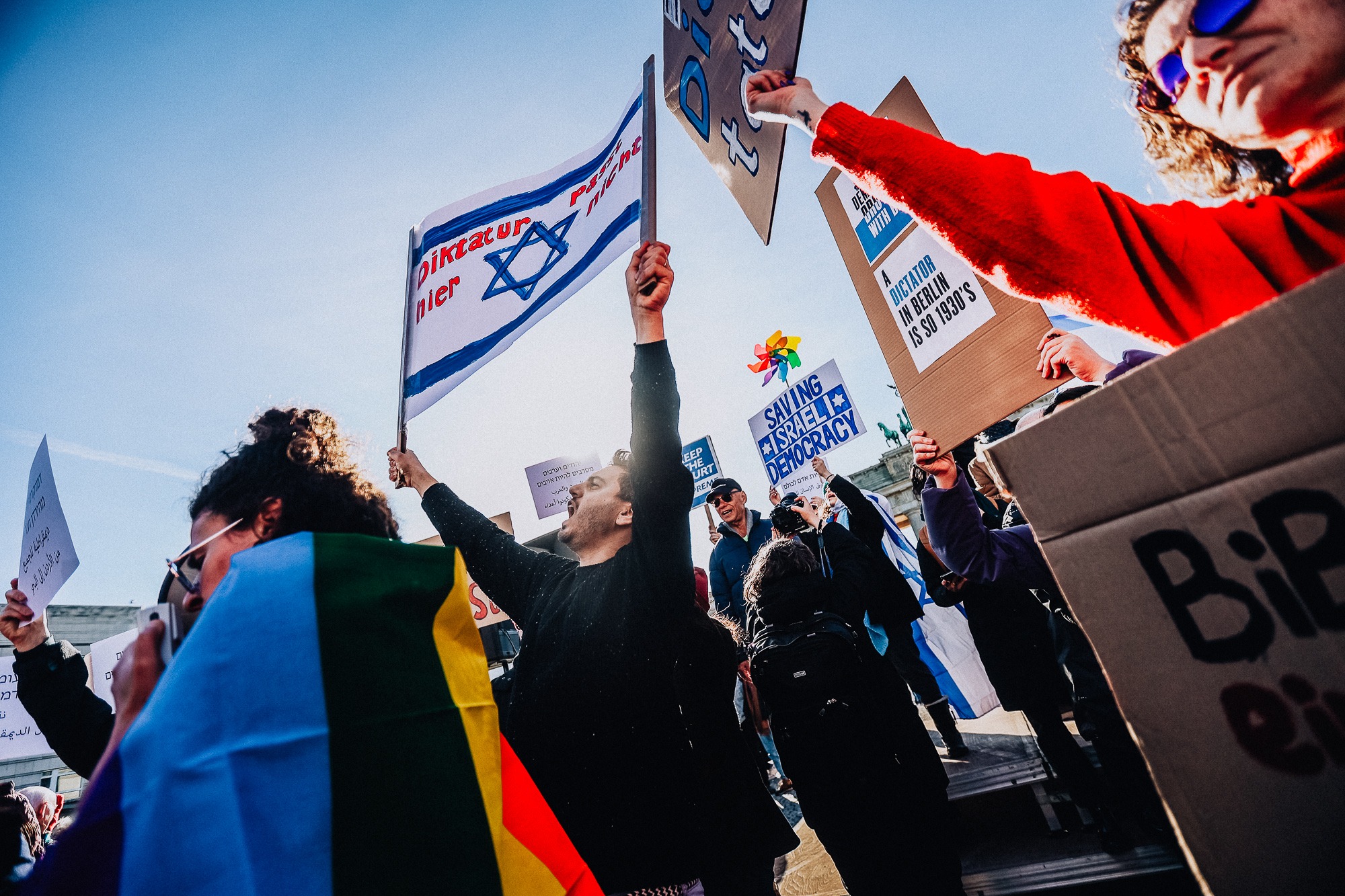 Das Foto zeigt eine Person mit einer israelischen Flagge in einer Menschenmenge. Im Hintergrund sieht man das Brandenburger Tor in Berlin. Das Foto wurde im Rahmen einer Demonstration gegen den Staatsbesuch des israelischen Ministerpräsidenten Benjamin Netanjahu in Berlin für die Bildagentur Getty Images aufgenommen.