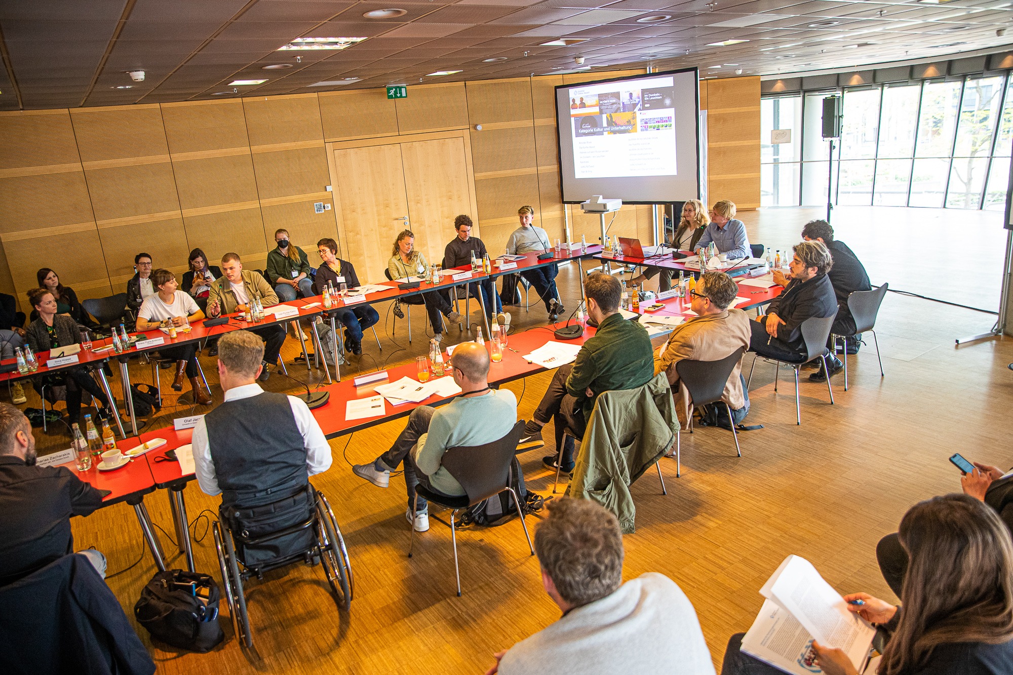 Das Bild zeigt einen großen Tisch mit Menschen. Die Veranstaltung ist die Vorstellung der Nominierten für den Grimme Online Award.