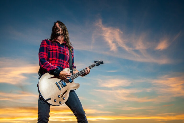 Ein Mann hält eine Gitarre vor einem Sonnenuntergang.